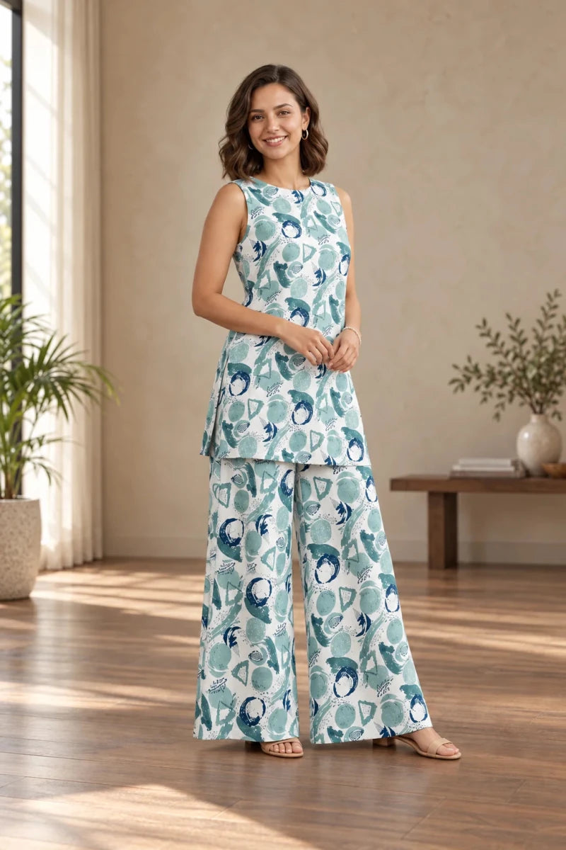 A woman modeling a sleeveless two-piece matching set with a peplum-style top and wide-leg pants, featuring a teal and white abstract pattern, in a warm-toned indoor room.