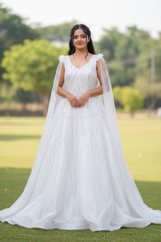 Woman in a white dress with a cape standing on grass with trees in the background
